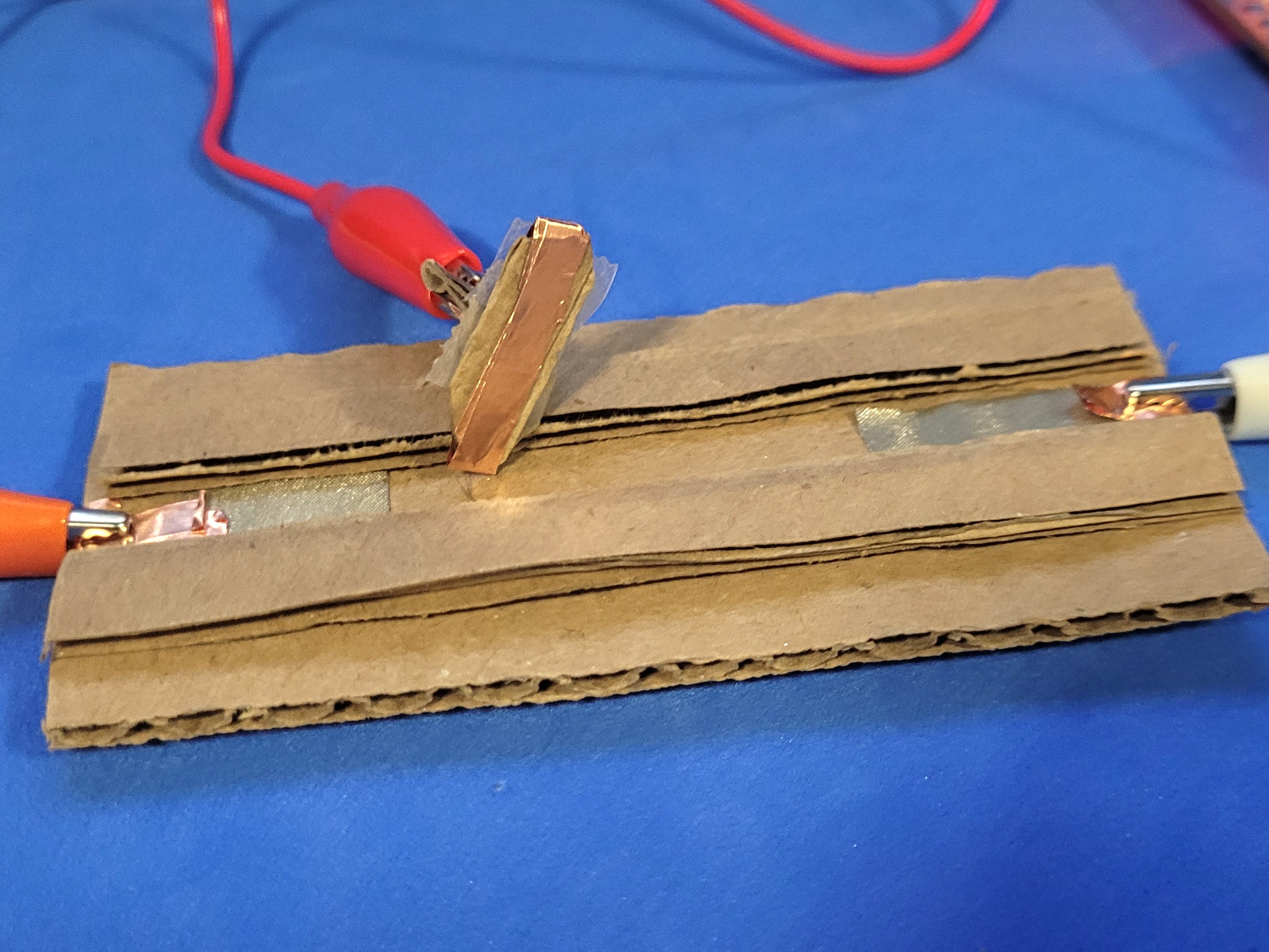 A photo of a created cardboard slider. Both sides correspond to different keys that will function as an on and off state for the circuit. The slider part acts as the ground to the MakeyMakey.