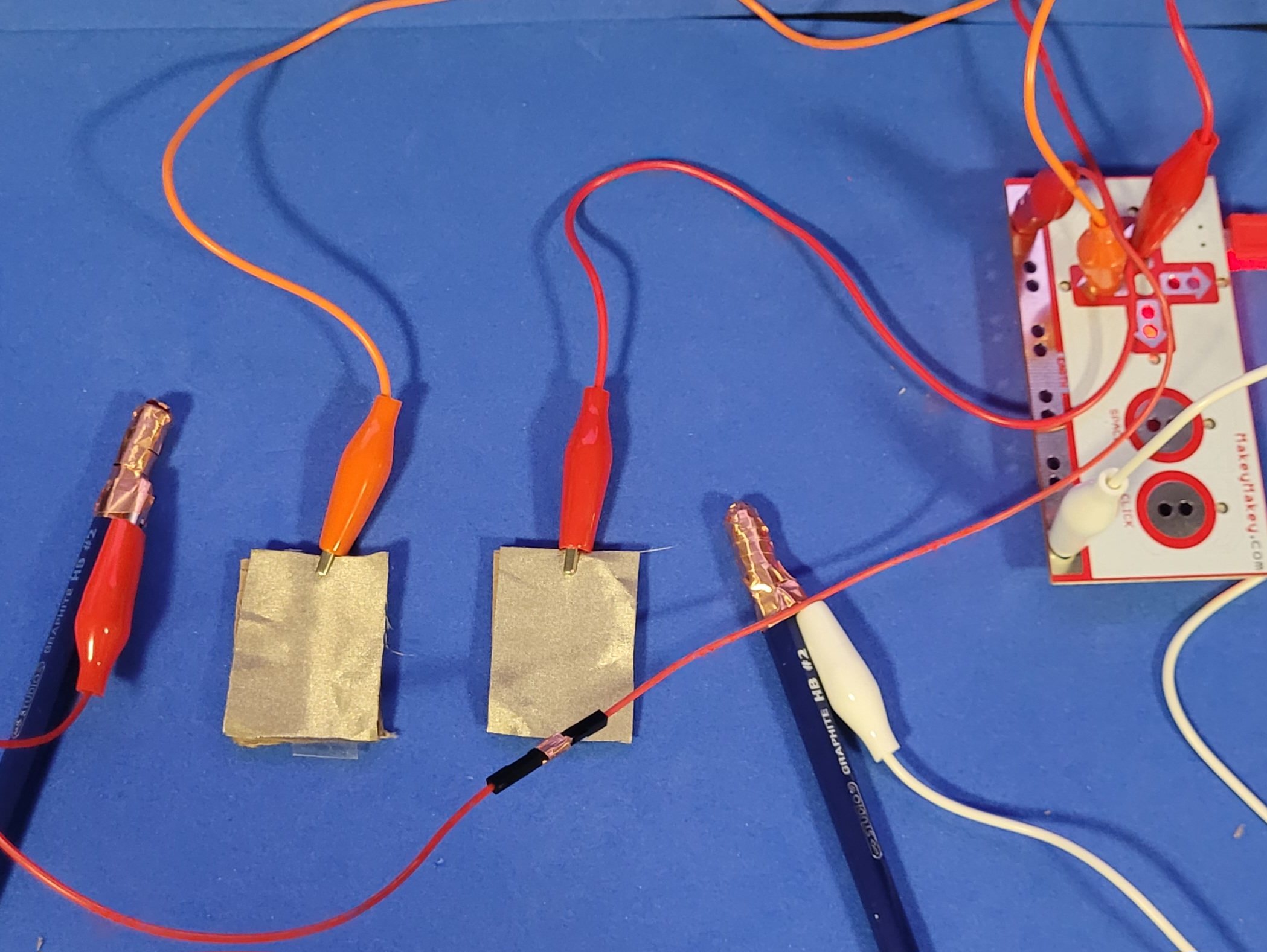 A photo displaying a demo of a drum type circuit with the pencils acting as the ground to the two key pieces of conductive fabric that correspond to key presses on the MakeyMakey